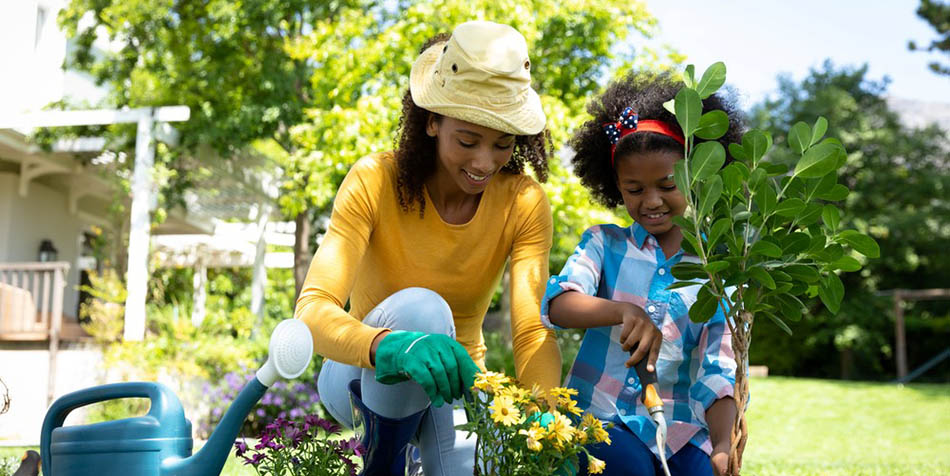 African American woman and her daughter in the garden, kneeling and potting plants.