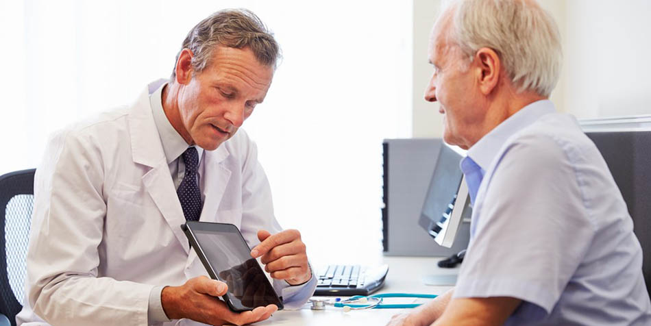 A doctor shows an older man test results on a tablet.
