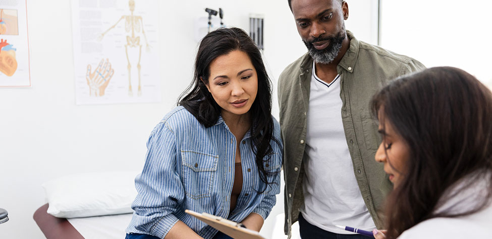 A male and female couple looks at a chart as a doctor explains test results.